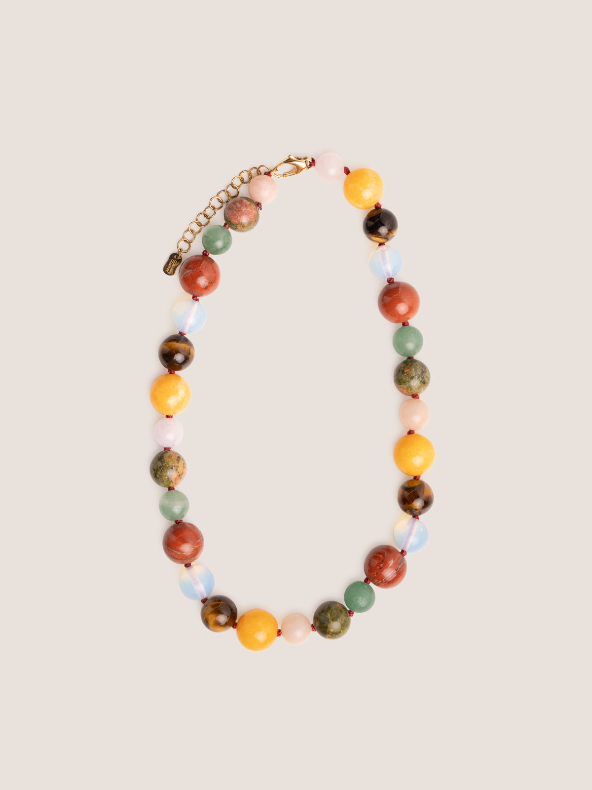 Collana Bold con pietre dure in diaspro rosso, giada gialla, occhio di tigre e opale, fotografia still life su sfondo neutro.