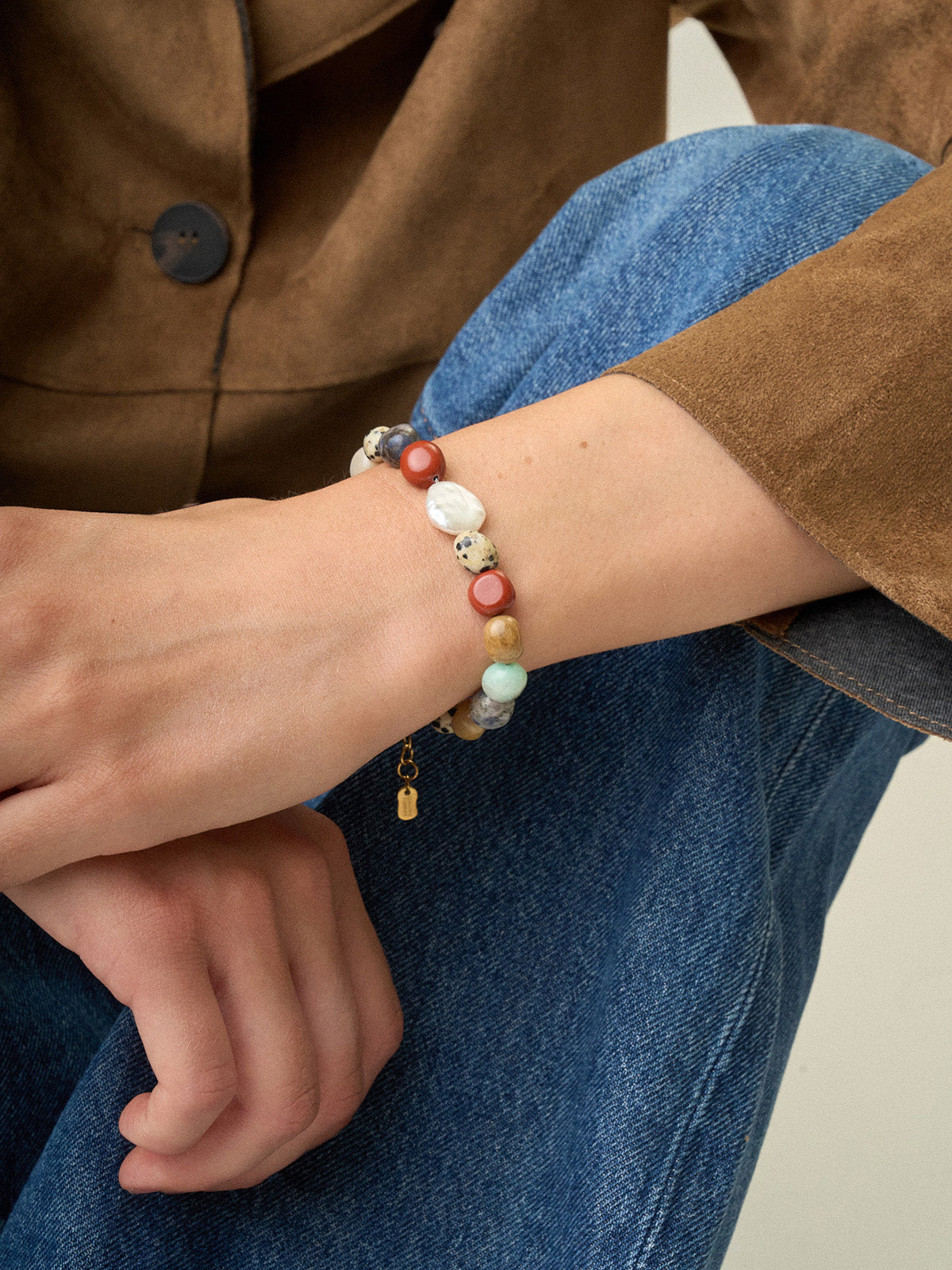 Ragazza che indossa un bracciale Bold con diaspro rosso, lapislazzuli, diaspro dalmata e perla centrale, fotografia close-up.