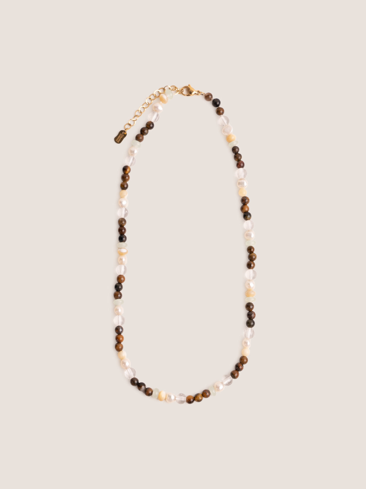 Collanina realizzata con un’alternanza di pietre dure tra cui occhio di tigre, madreperla, new jade e perle di fiume foto su sfondo bianco.
