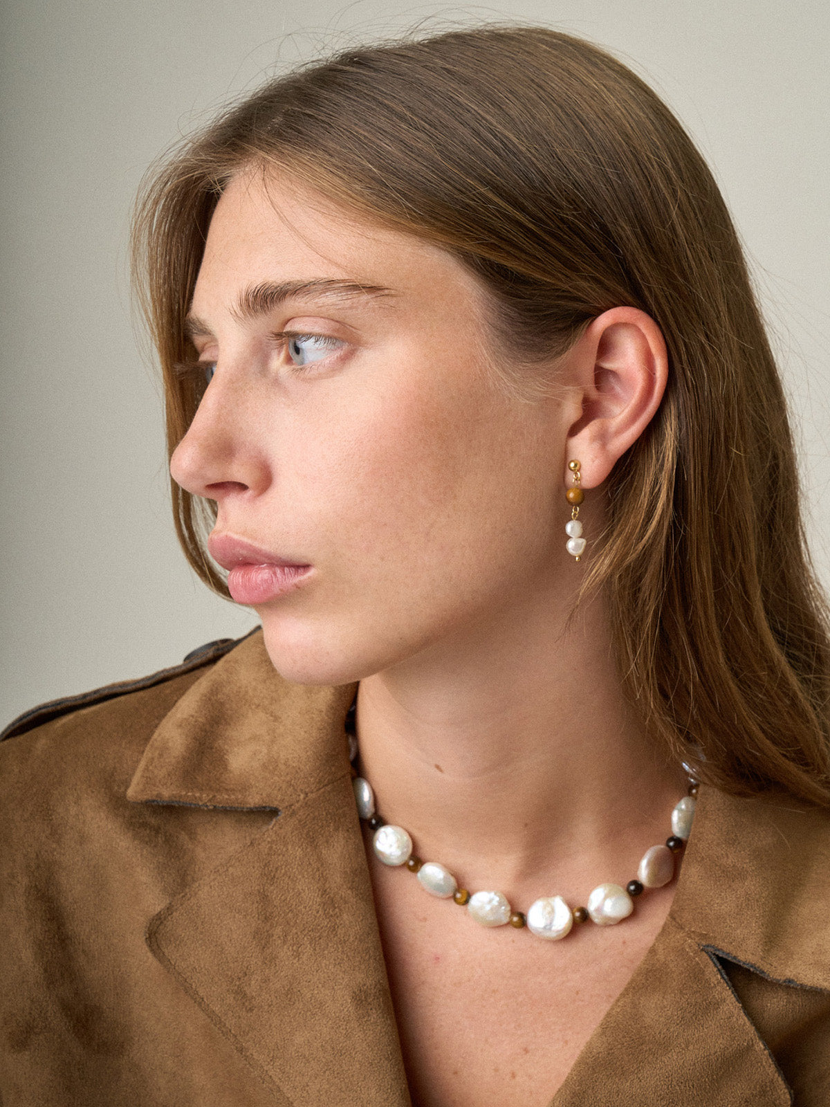 Ragazza che indossa una collanina Bold con occhio di tigre e perle rotonde, fotografia close-up.