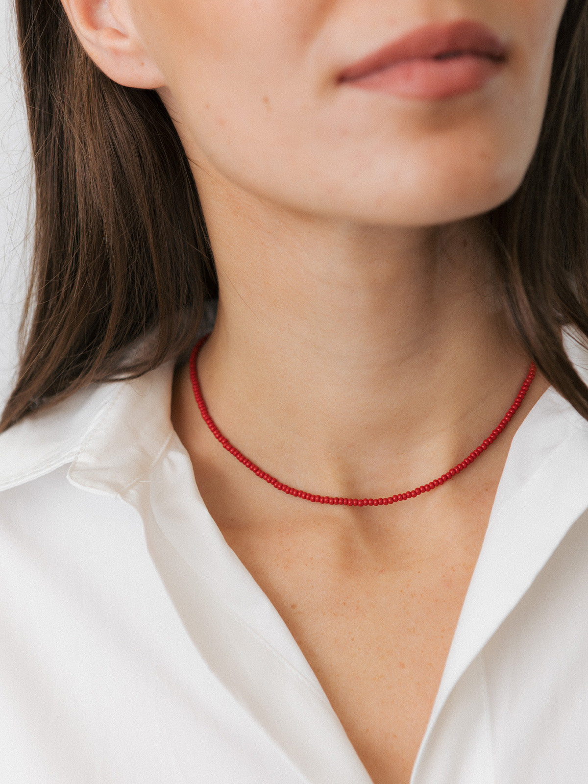 Ragazza che indossa una collanina con perline mini di vetro rosse e dettagli color oro, fotografia close-up.