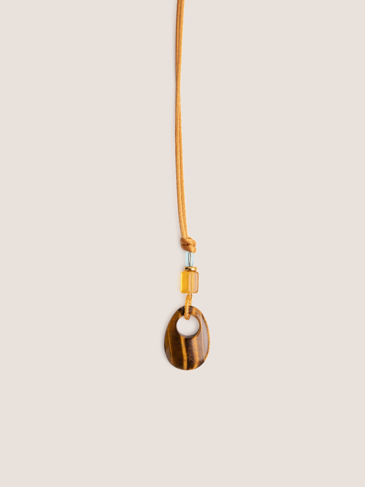 Collana con cordino in raso oro, vetri vintage e occhio di tigre, fotografia still life su sfondo neutro.