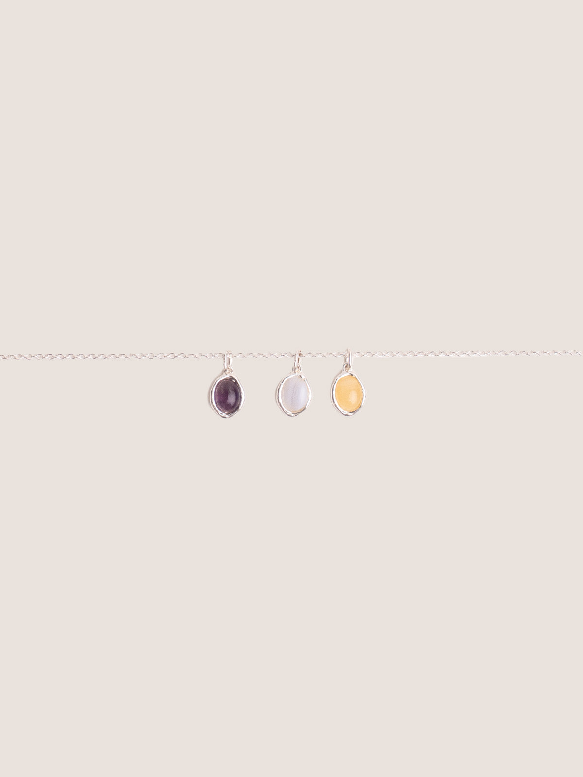 Catenina forzatina in argento con ciondoli Pietre della Nascita in ametista, pietra di luna e new jade, fotografia still life su sfondo neutro.