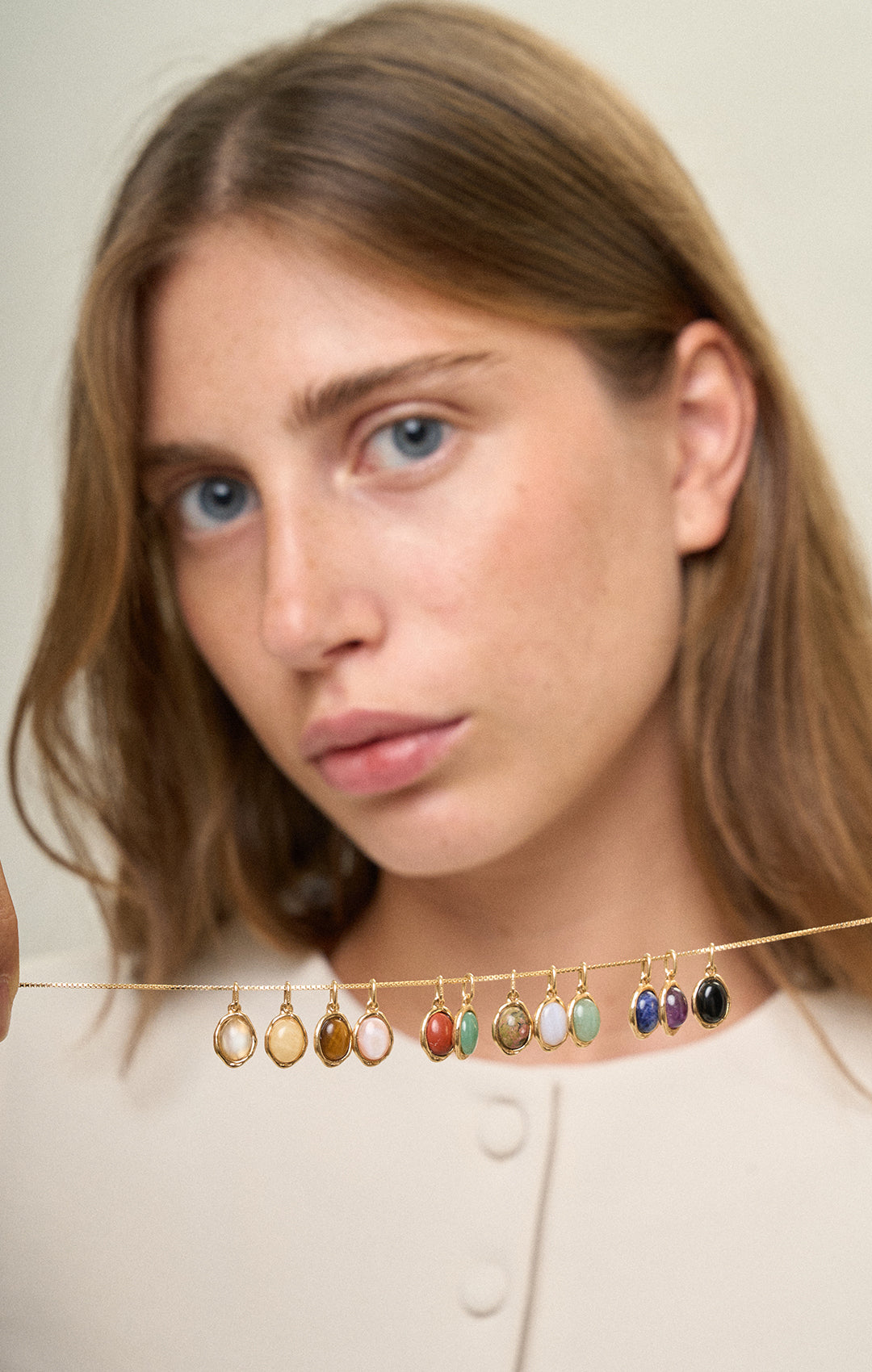 Ragazza che tiene in mano una catenina veneziana color oro con dodici ciondoli Pietre della Nascita, uno per ogni mese dell’anno, fotografia lifestyle