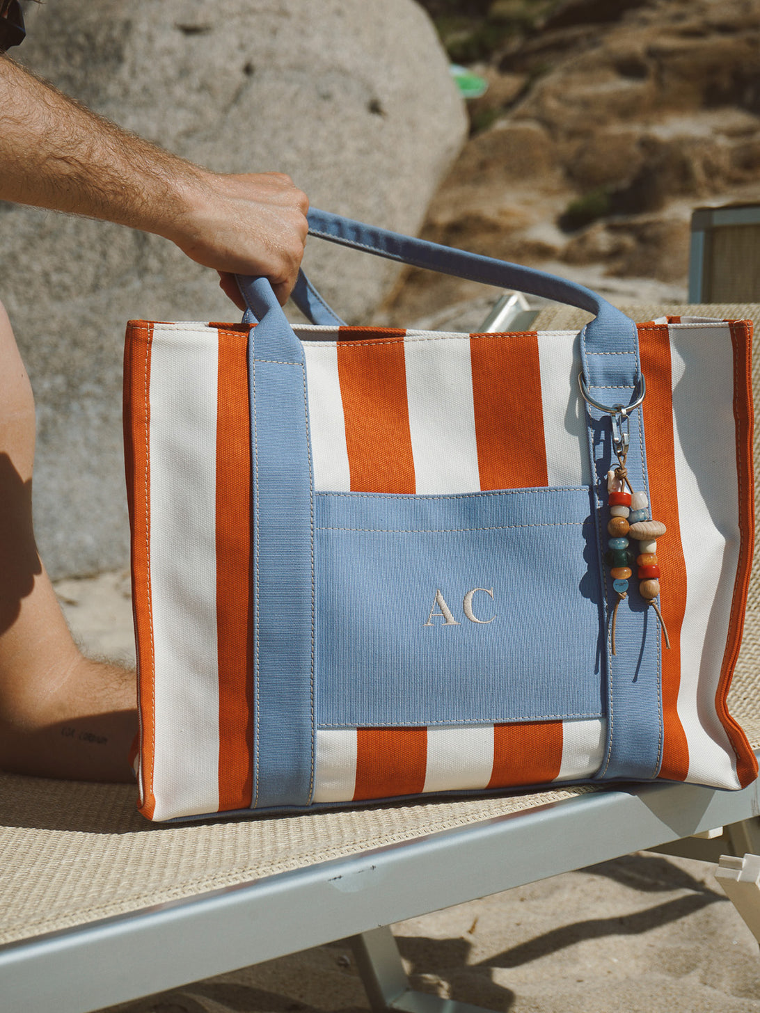 Ragazzo che tiene una borsa My Style Bags x Collanine Colorate a righe arancioni e bianche su un lettino da spiaggia