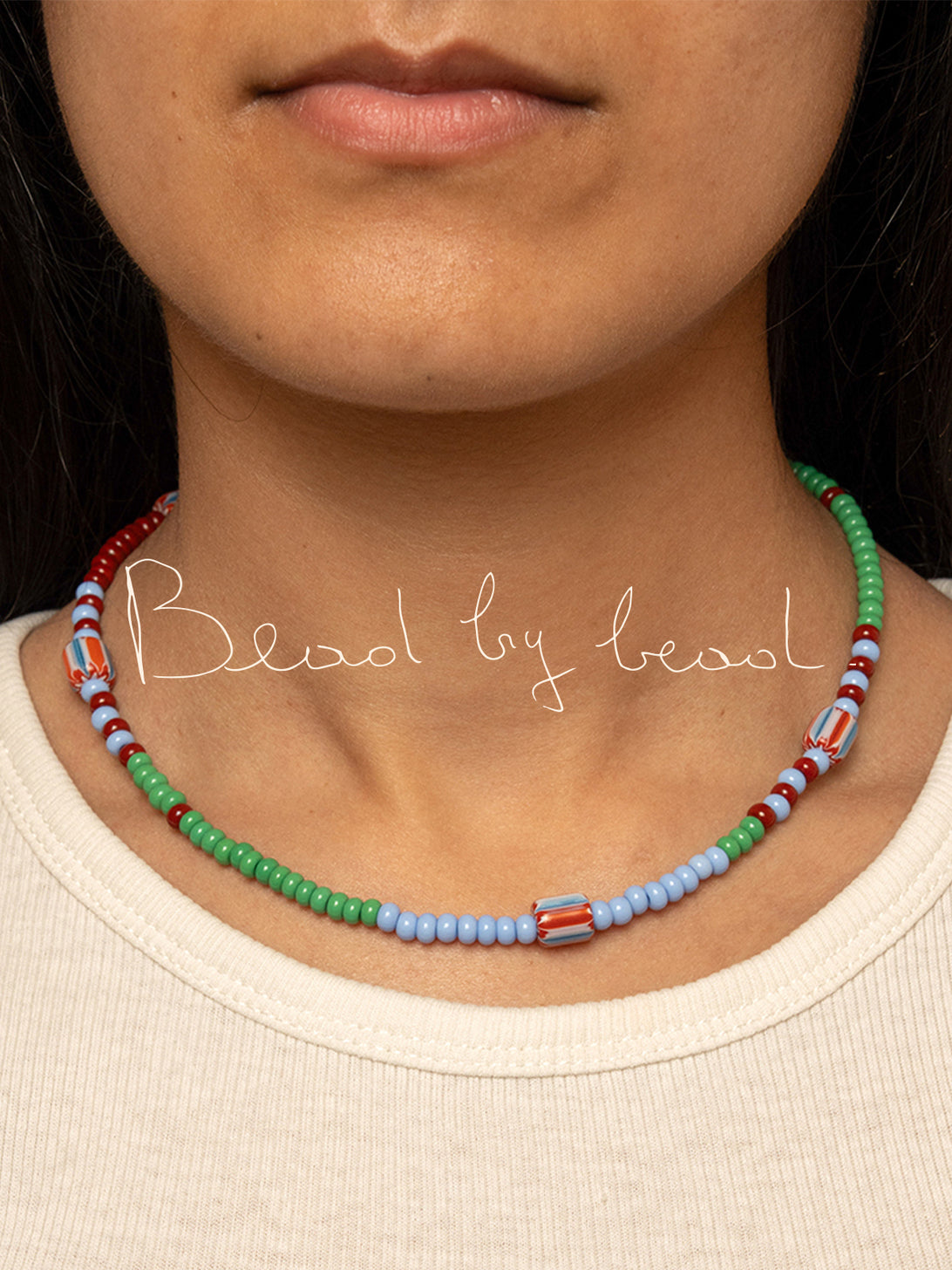 Ragazza che indossa la collanina Bead Multi della collezione Bead by Bead di Okapia x Collanine Colorate, con logo Bead by Bead in sovrimpressione, fotografia close-up delle perline di vetro multicolore