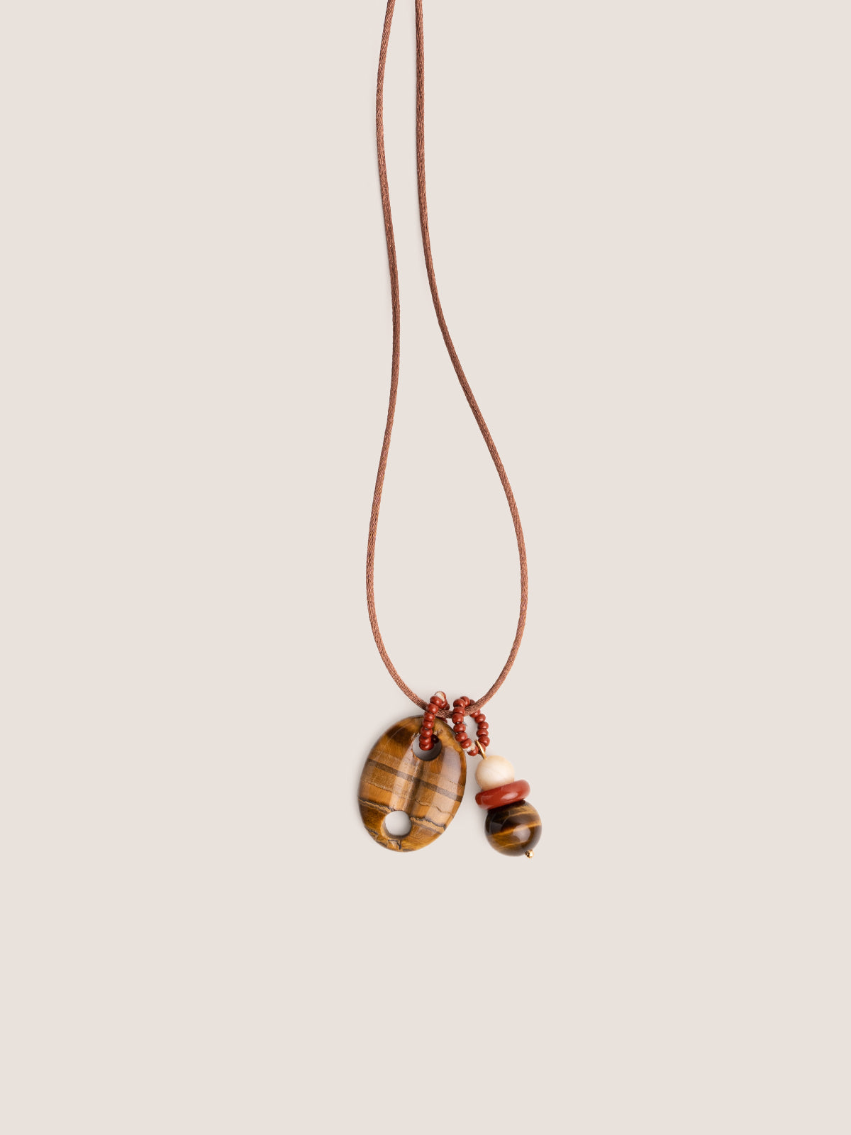 Collana con cordino in raso oro, maglia nautica in occhio di tigre e dettaglio in pietre dure, fotografia still life su sfondo neutro.