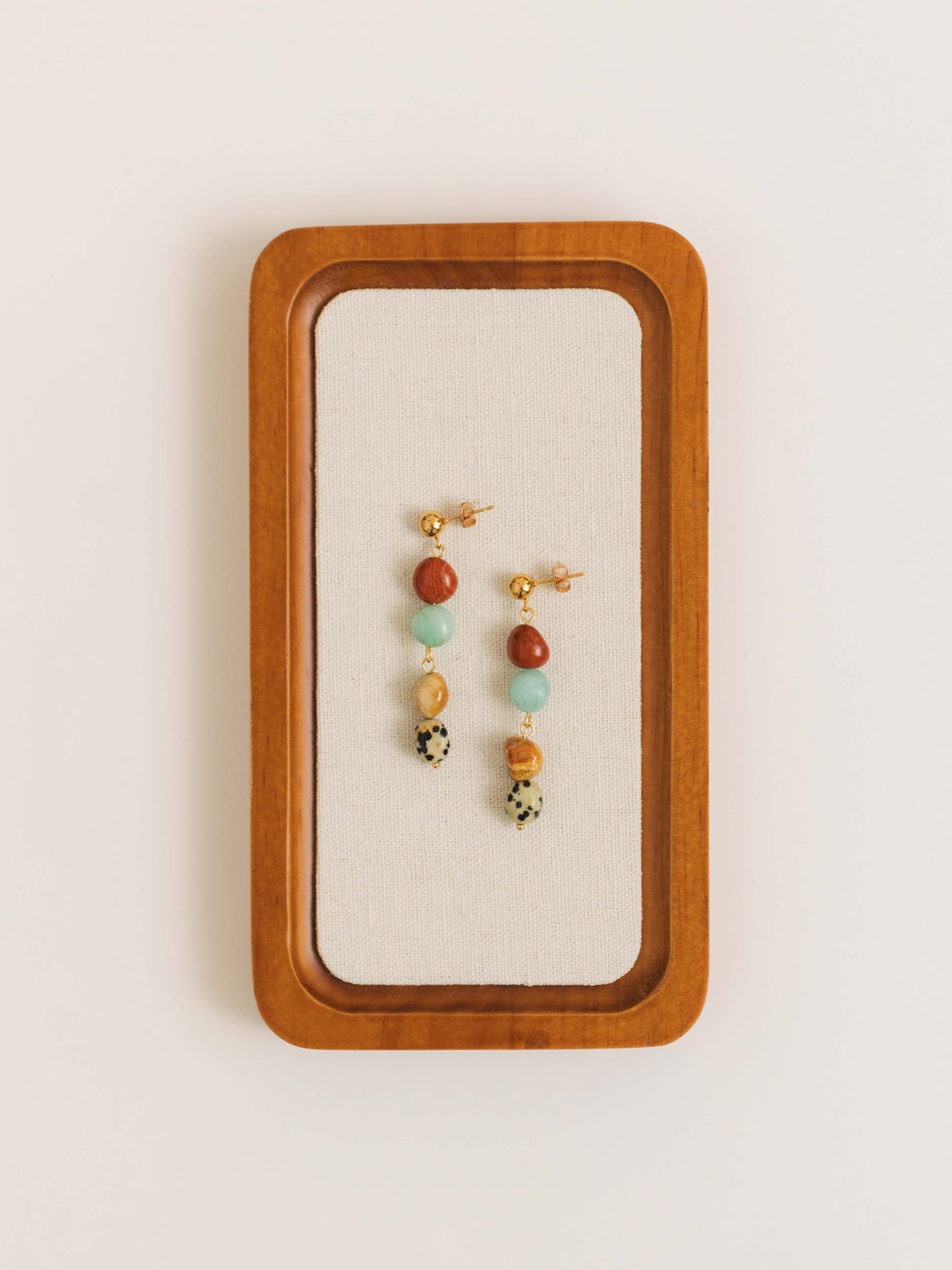 Orecchini con pietre dure in diaspro rosso, lapislazzuli, diaspro dalmata e amazzonite, fotografia still life creativa con vassoio in tessuto e legno.